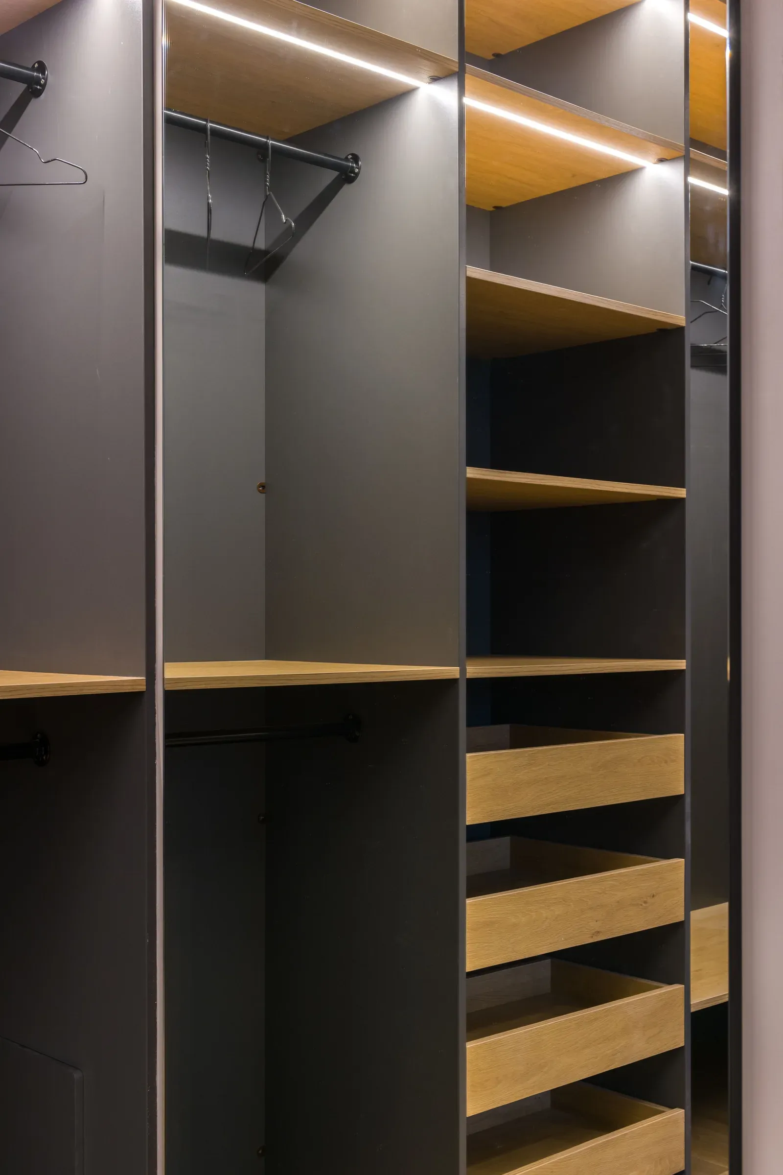 Grey walk-in wardrobe with oak shelves, pull-out drawers, hanging rails and LED strip lights