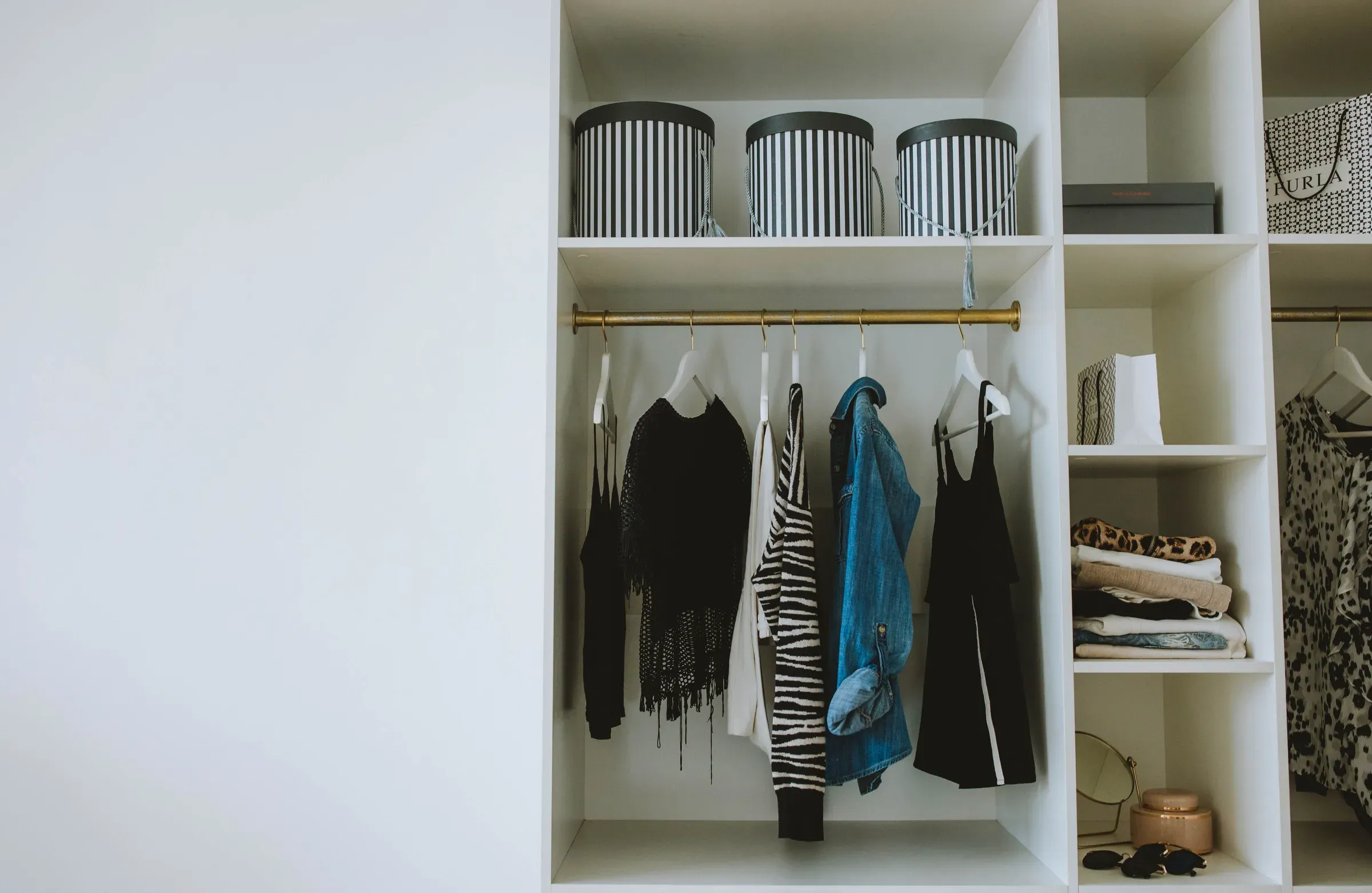 Open white wardrobe with a brass hanging rail, clothes, folded shelves and striped hat boxes