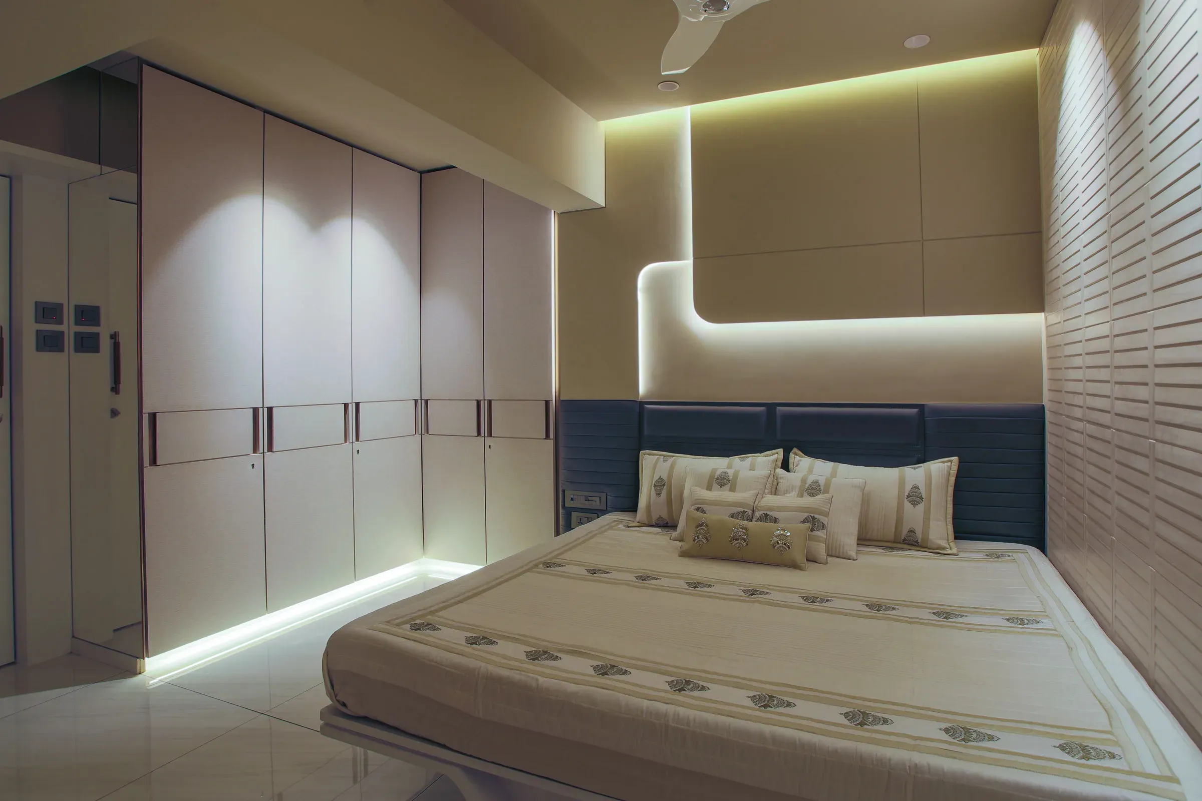 Bedroom with a floor-to-ceiling white wardrobe, LED plinth light, blue headboard and lit wall panel
